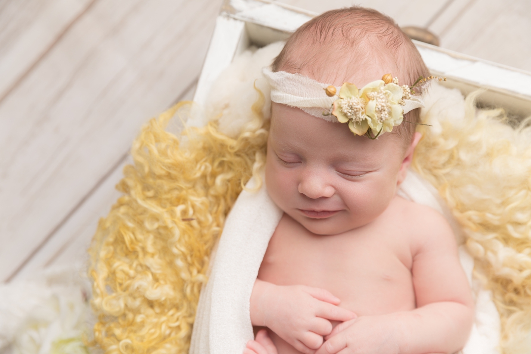 Newborn Photography worcestershire Hayley morris. Baby partially wrapped in a bed prop, smiling with a pretty headband. 